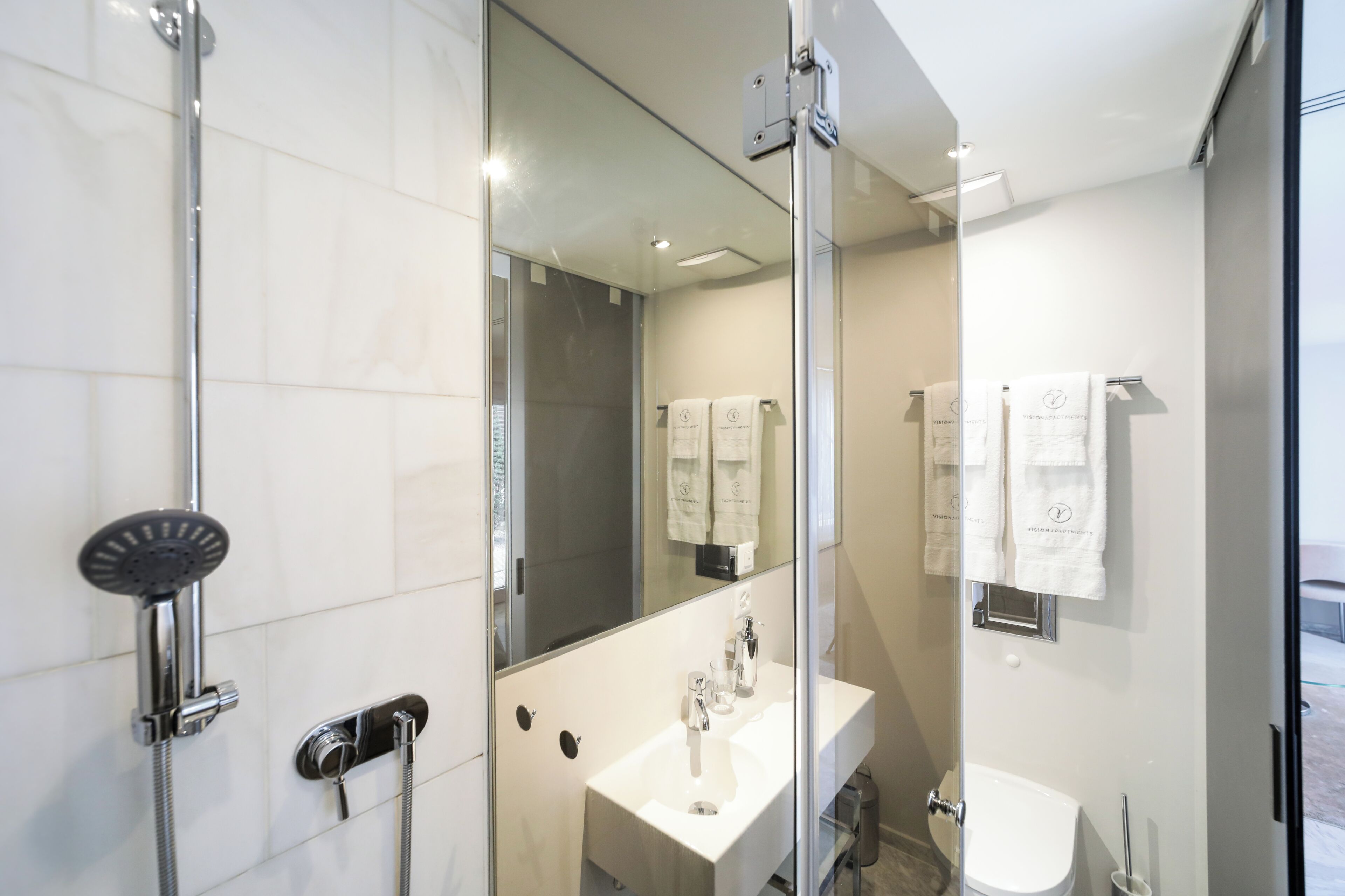 Une salle de bain moderne avec une douche à parois de verre, un lavabo blanc et un miroir qui reflète les serviettes.