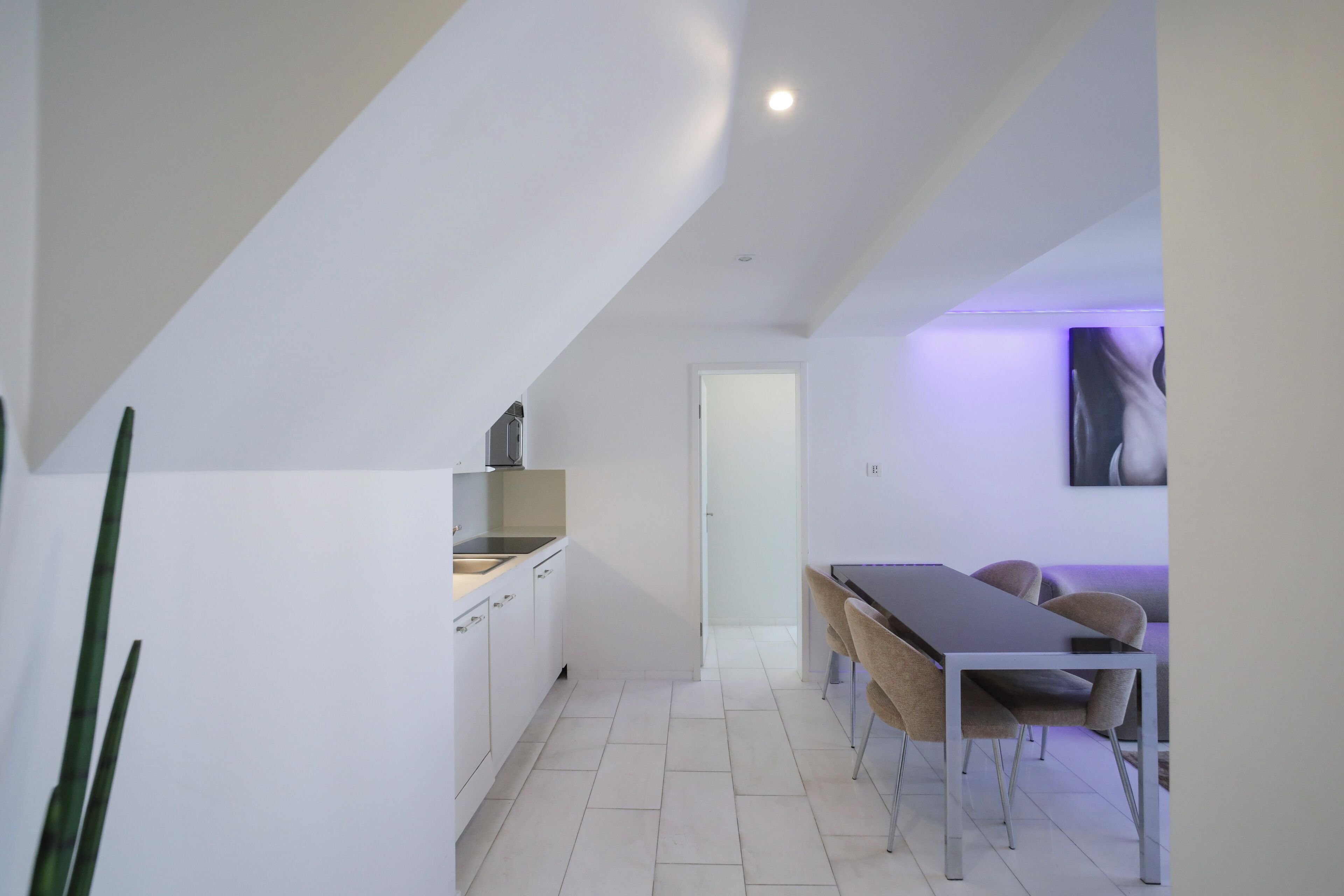 Une cuisine moderne avec des meubles blancs et un four encastré, qui donne sur un coin repas avec une longue table et des chaises.