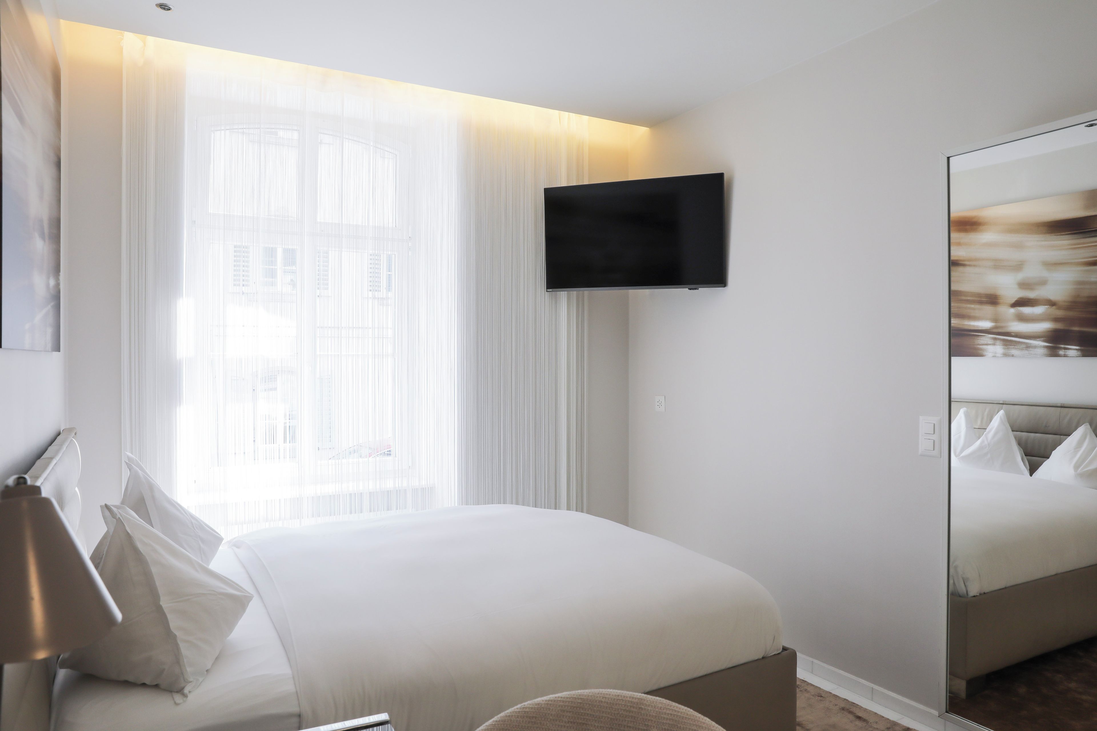 Ein Hotelzimmer mit einem Bett, einem flachbildfernseher an der Wand und einem großen Spiegel, der das Bett wiederspiegelt.