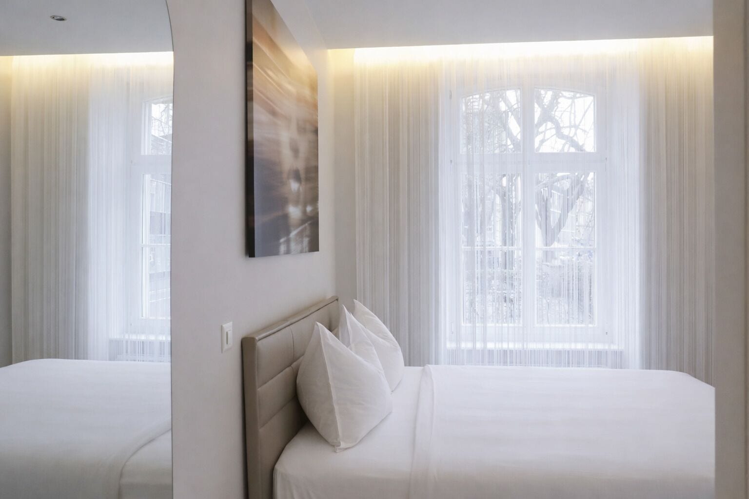 Een hotelkamer met een groot bed, een hoofdeinde en een raam met dunne gordijnen.