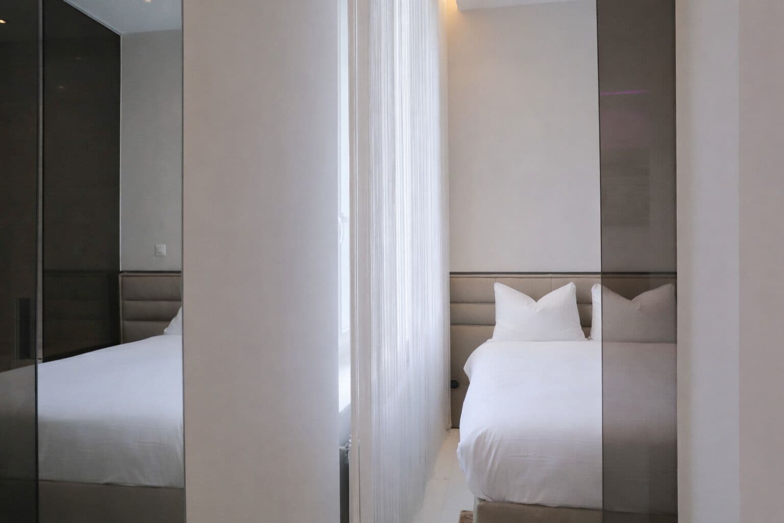 A modern hotel room with a large mirror, a bed with white linens, and a neutral color palette.