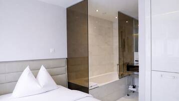 Ein modernes Hotelzimmer mit Bett, einer gläsernen Dusche und einem weißen Kleiderschrank.