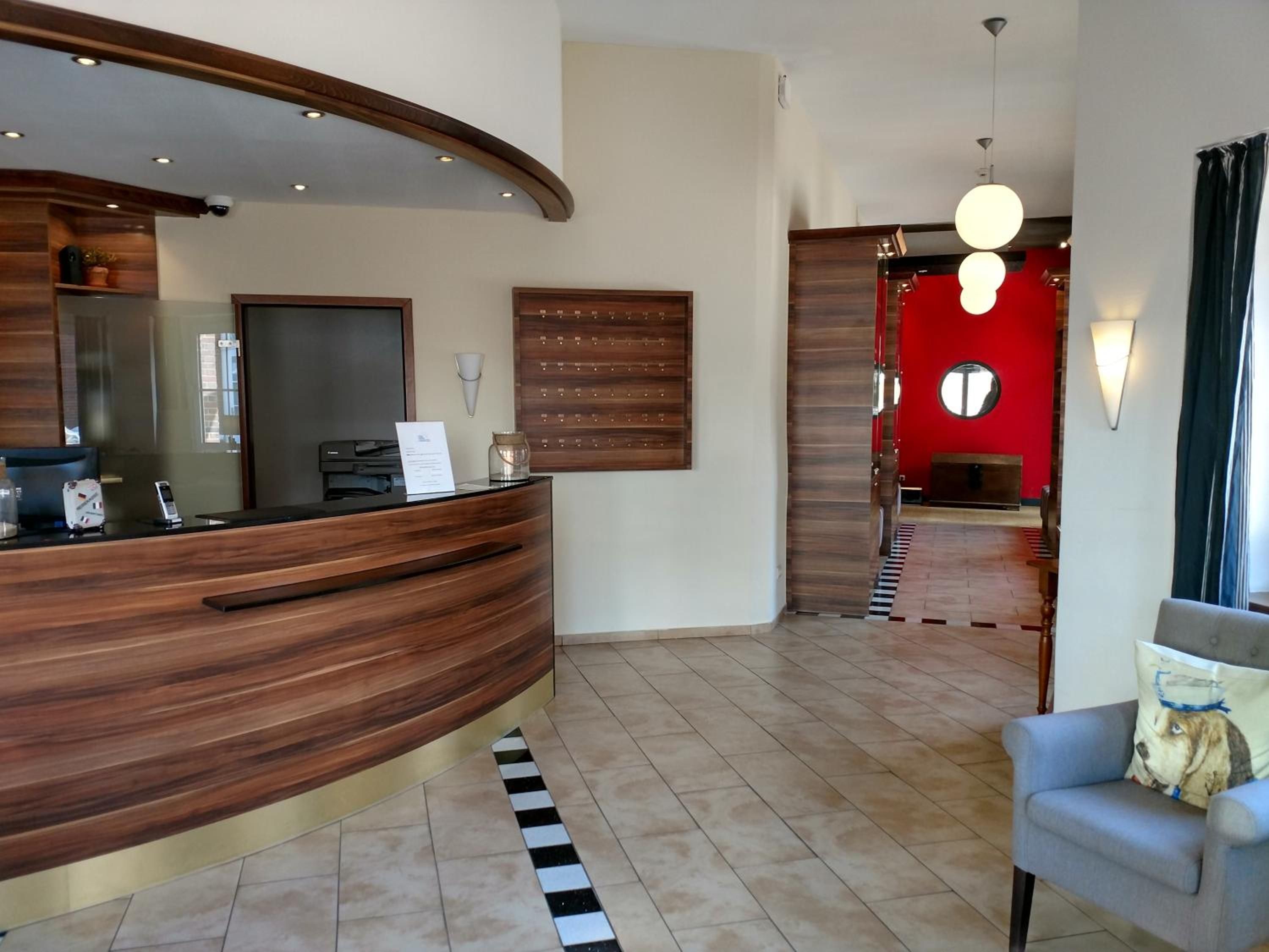 A reception area with a wooden reception desk, a mirror, a wall-mounted light, and a red accent wall.