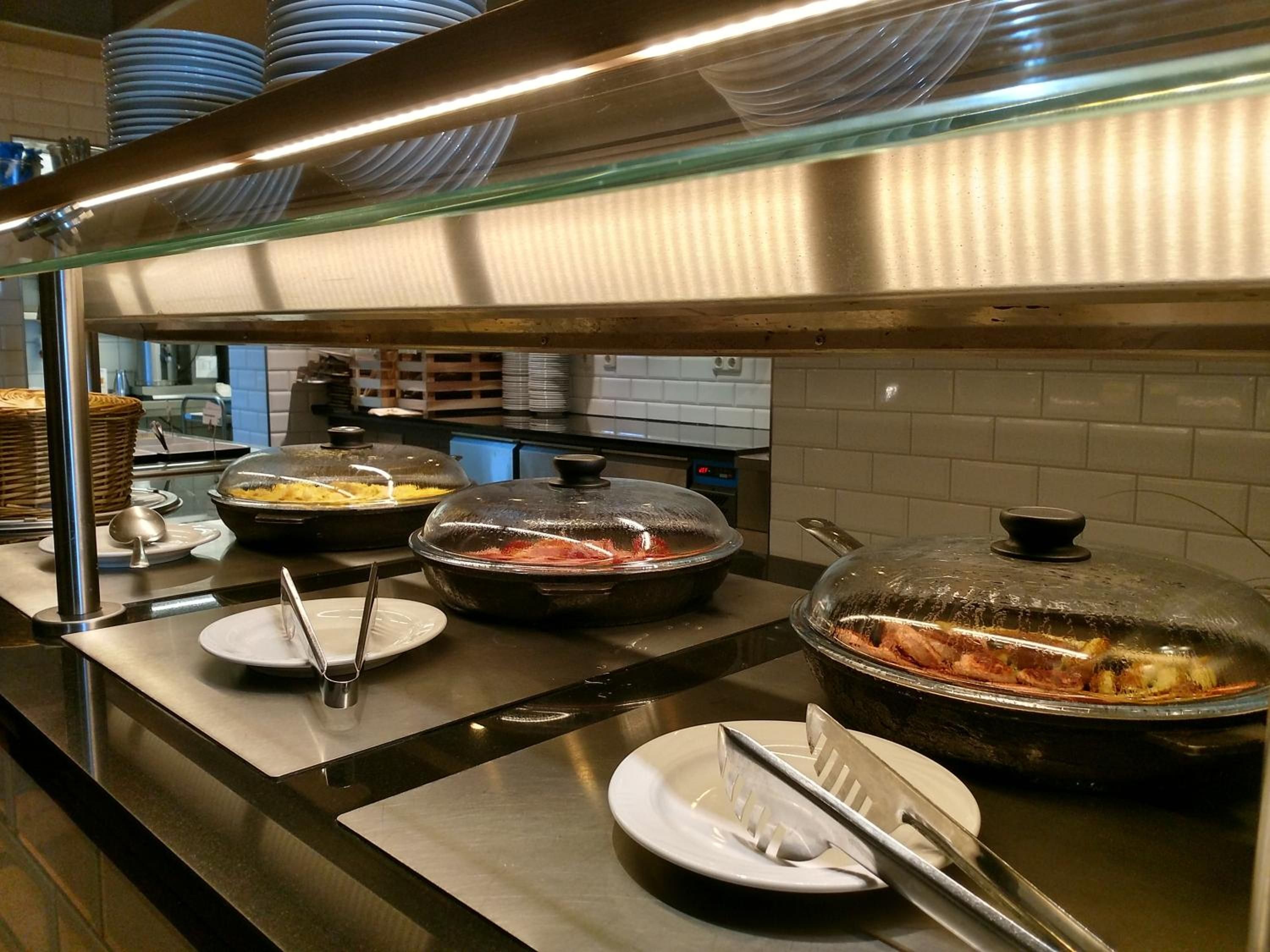 A buffet setup with covered food containers, serving utensils, and stacked plates.