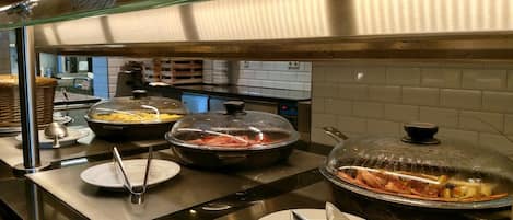 A buffet setup with covered food containers, serving utensils, and stacked plates.