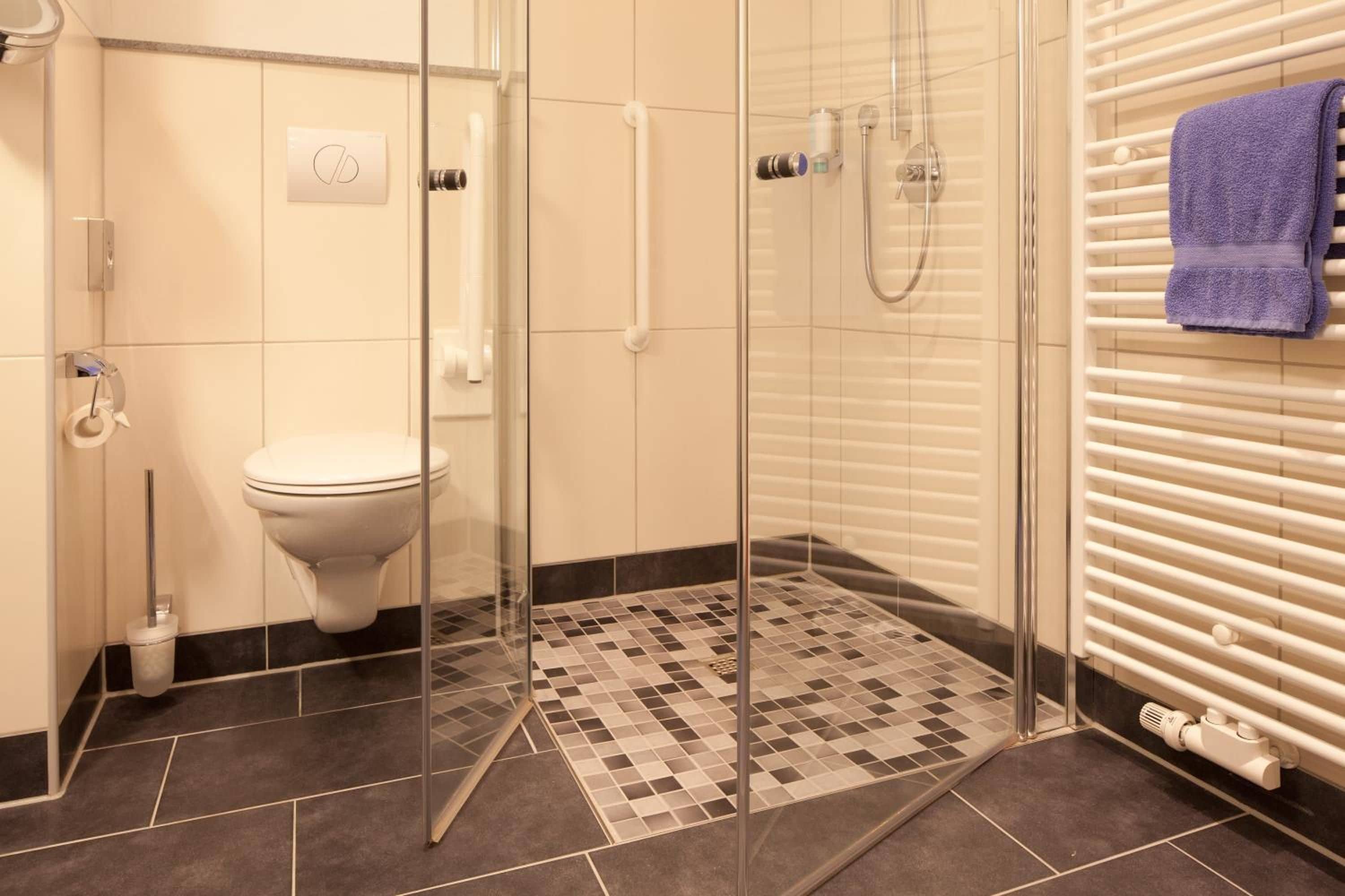 A modern bathroom with a glass shower enclosure, a toilet, and a towel rack with a towel.