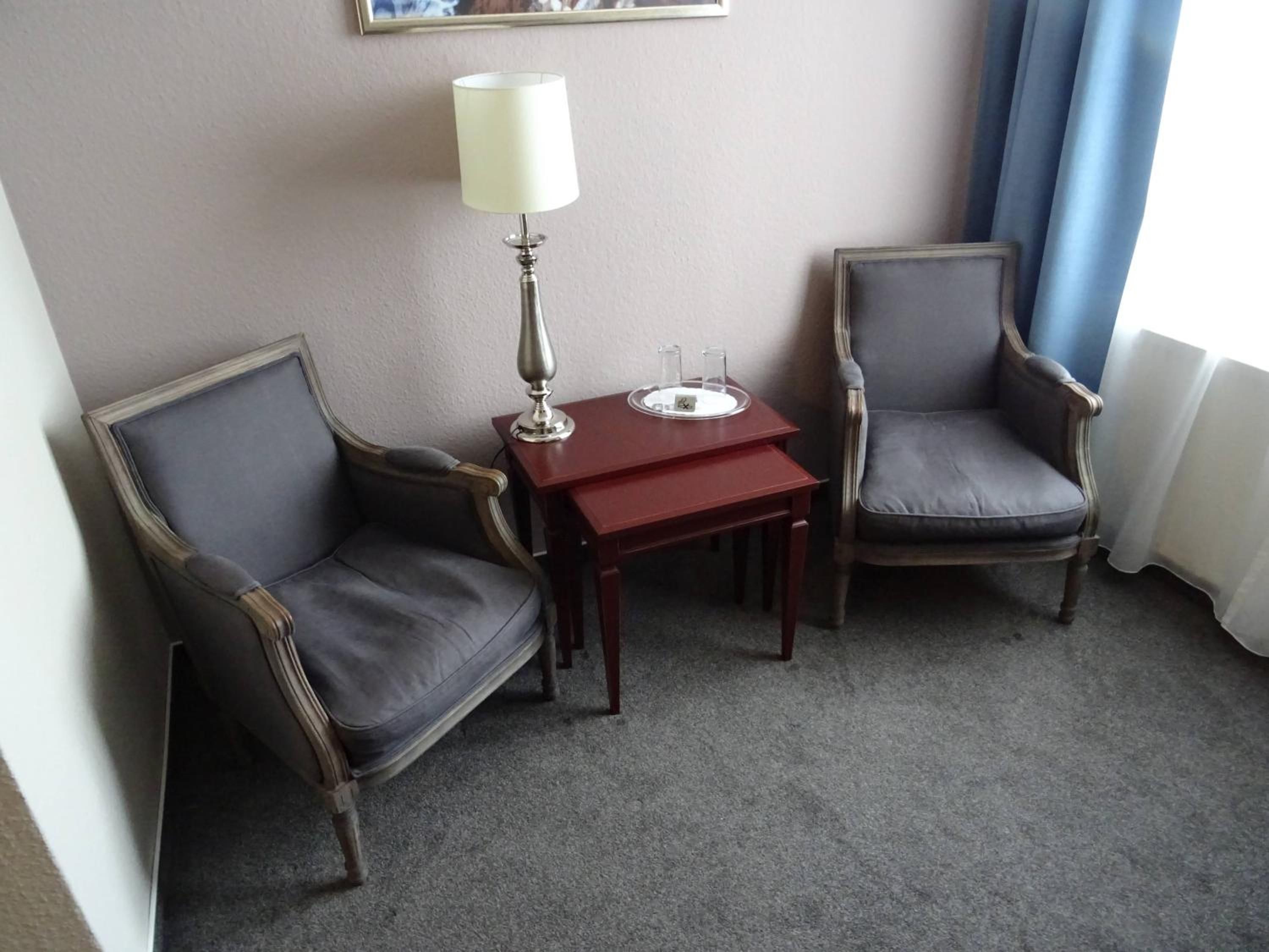 Een hotelkamer met twee fauteuils, een tafeltje met een lamp en een raam met gordijnen.