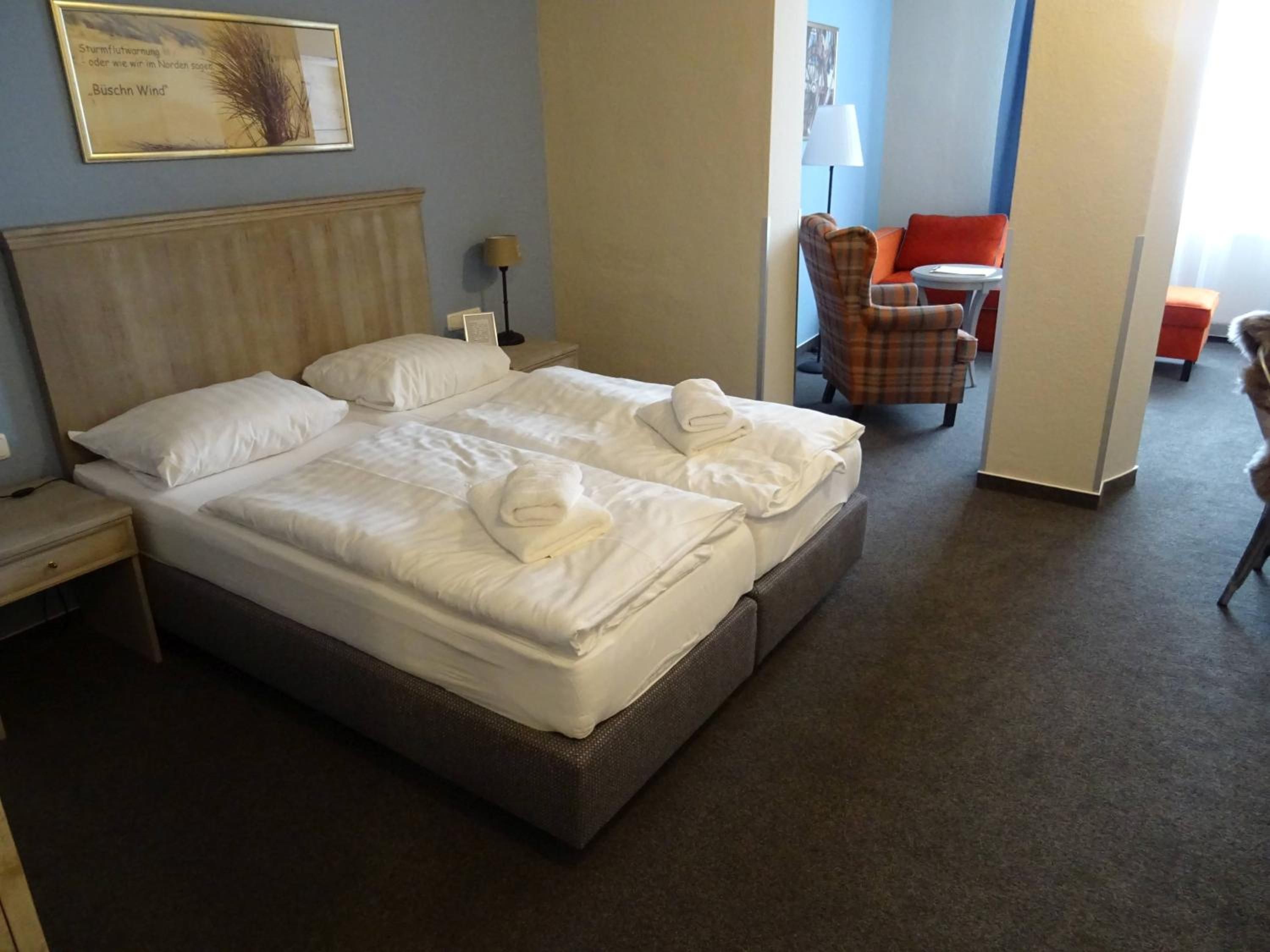 A hotel room with a large bed, two pillows, a bedside table, a lamp, and a chair.