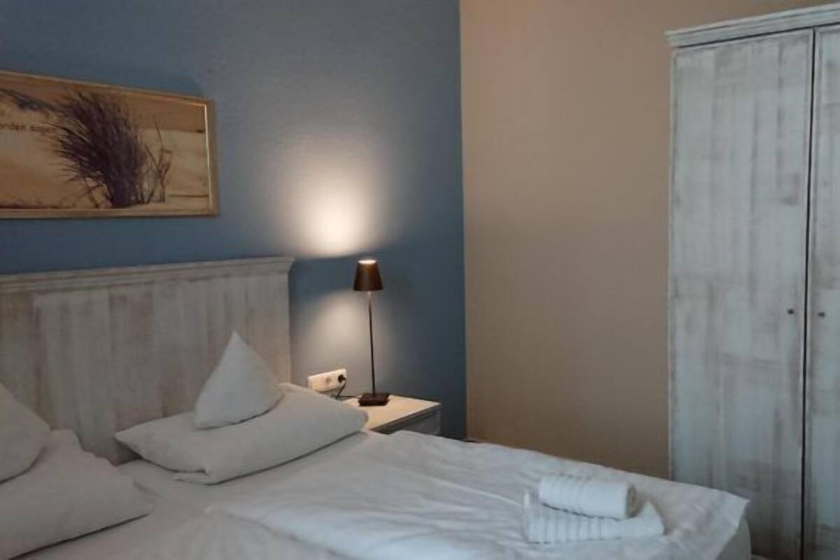 A bedroom with a bed, pillows, a nightstand, a lamp, and a wardrobe.