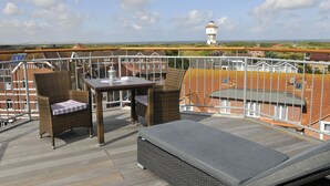 Ein Balkon mit Korbmöbeln, einem Tisch und Blick auf einen Leuchtturm in der Ferne.