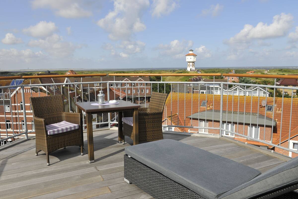 A balcony with wicker furniture, a table, and a view of a lighthouse in the distance.