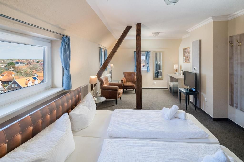 A hotel room with two beds, a sitting area with chairs, a television, and a view of the outside.