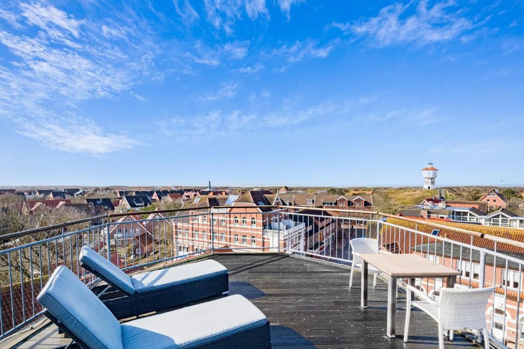 Une terrasse sur le toit, dotée de chaises longues et d’une table, offrant une vue sur un quartier résidentiel avec ses maisons et son phare.
