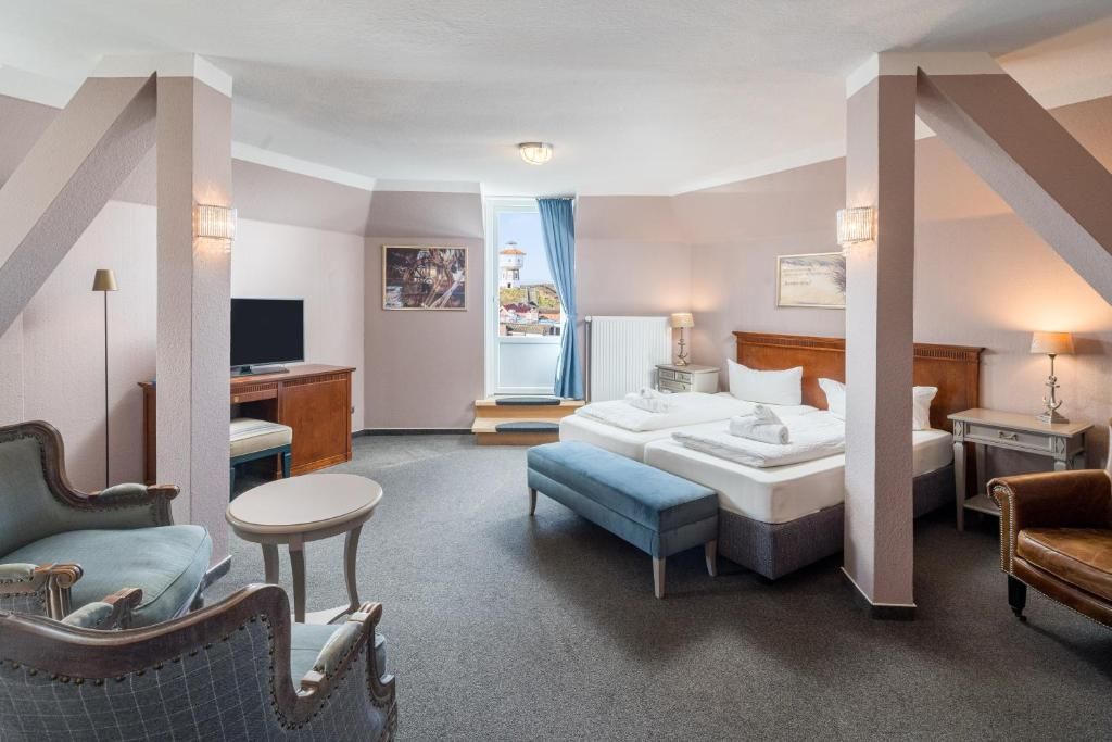 A hotel room with a bed, a desk, a chair, a small table, and a television.