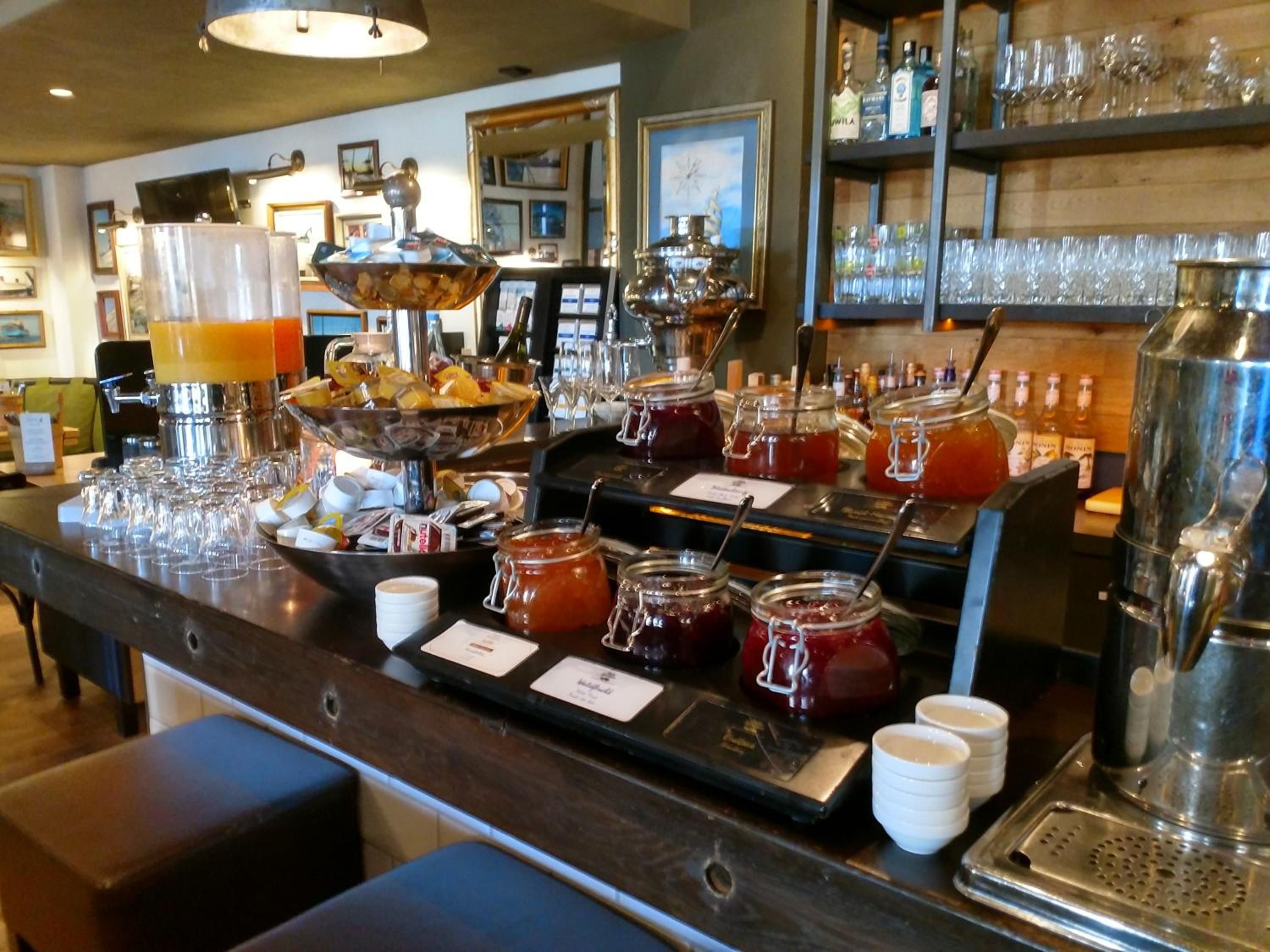 Un espace bar proposant une variété de boissons, notamment un distributeur de punch aux fruits, une machine à café et plusieurs pots de confiture.