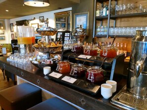 A bar area with a variety of beverages, including a fruit punch dispenser, a coffee machine, and several jars of jam. - Inselhotel Langeoog (Langeoog)