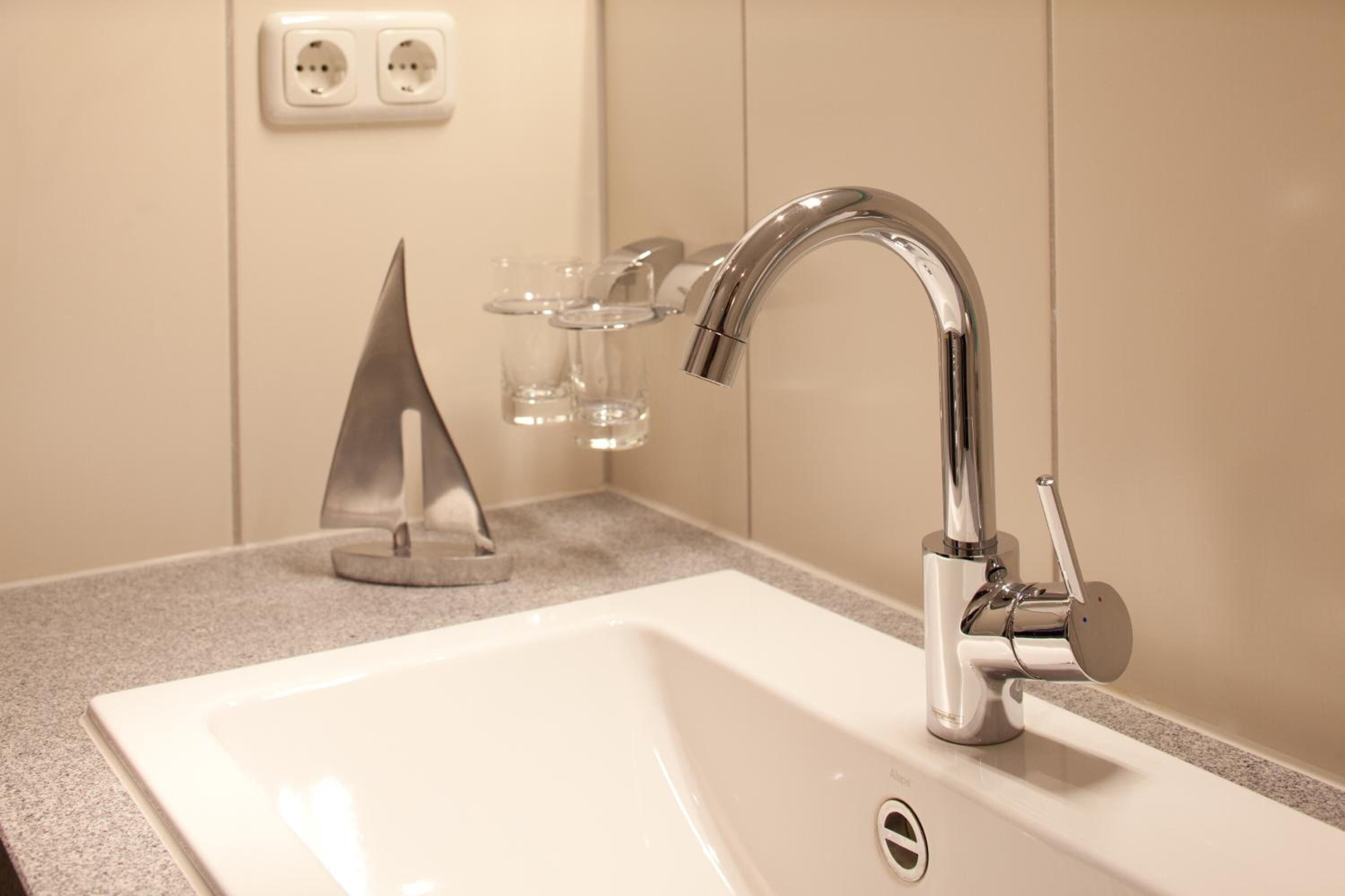 A modern bathroom with a chrome faucet, a white sink, and a glass candle holder.