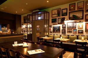A restaurant with wooden tables and booths, framed pictures on the walls, and a ship model on the ceiling. - Inselhotel Langeoog (Langeoog)