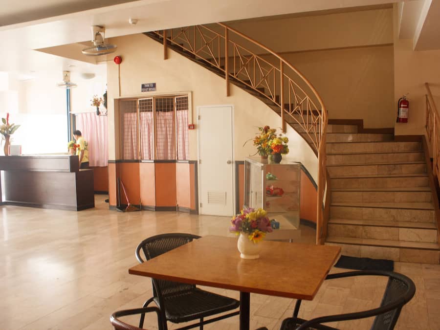 Eine Hotelhalle mit einer Rezeption, einer Treppe und einem Essbereich mit Tisch und Stühlen.