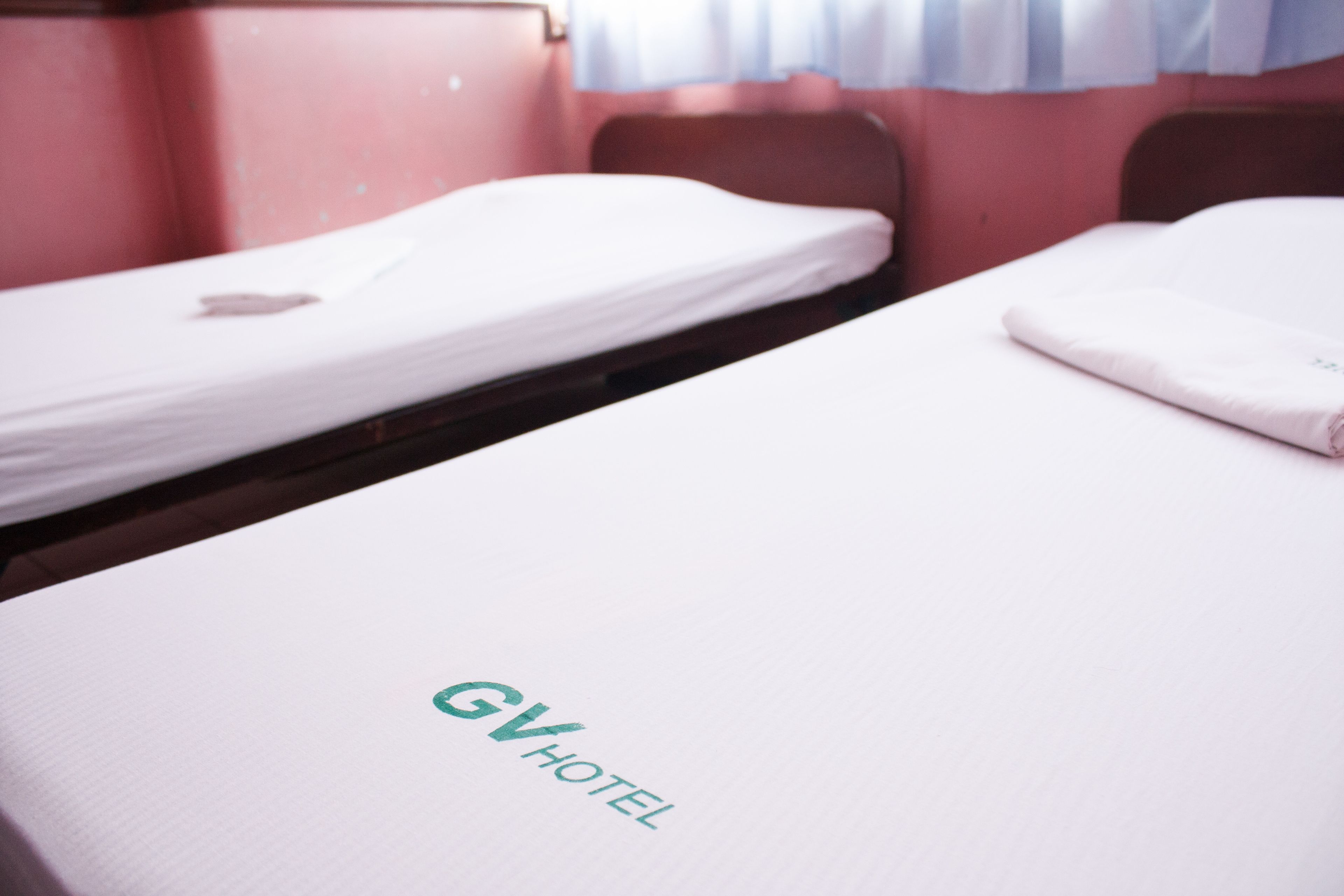 Un lit simple avec un matelas blanc et une tête de lit, portant l’inscription « GV HOTEL ».