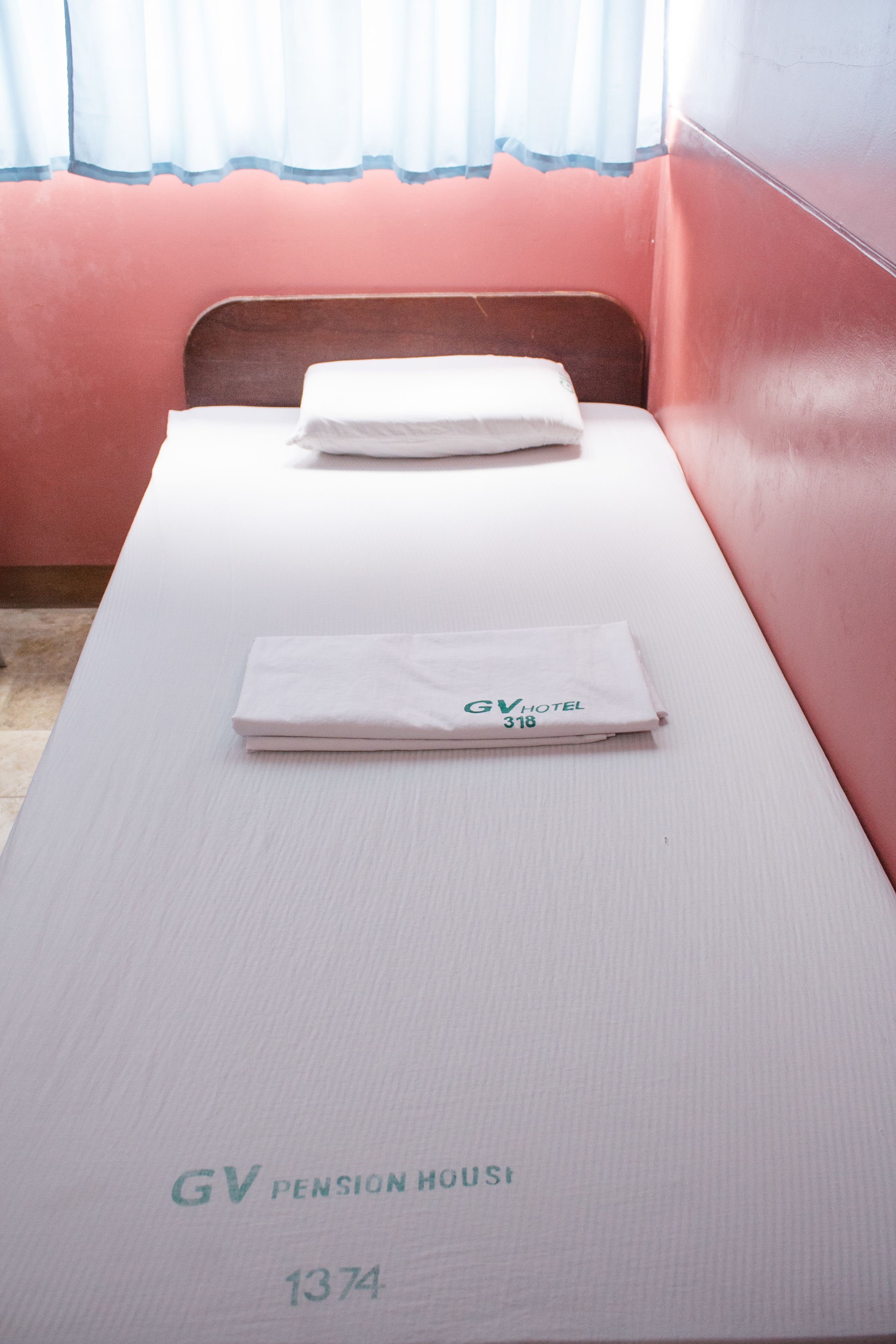 Een enkel bed in een kamer met een witte matras en een opgevouwen witte handdoek erop. Het bed is aangeduid met 