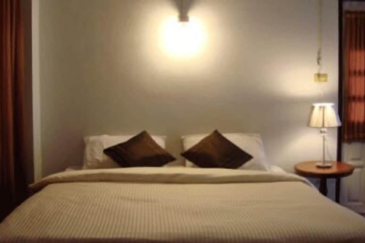 A hotel room with a bed, two pillows, a bedside lamp, and a wall-mounted light.