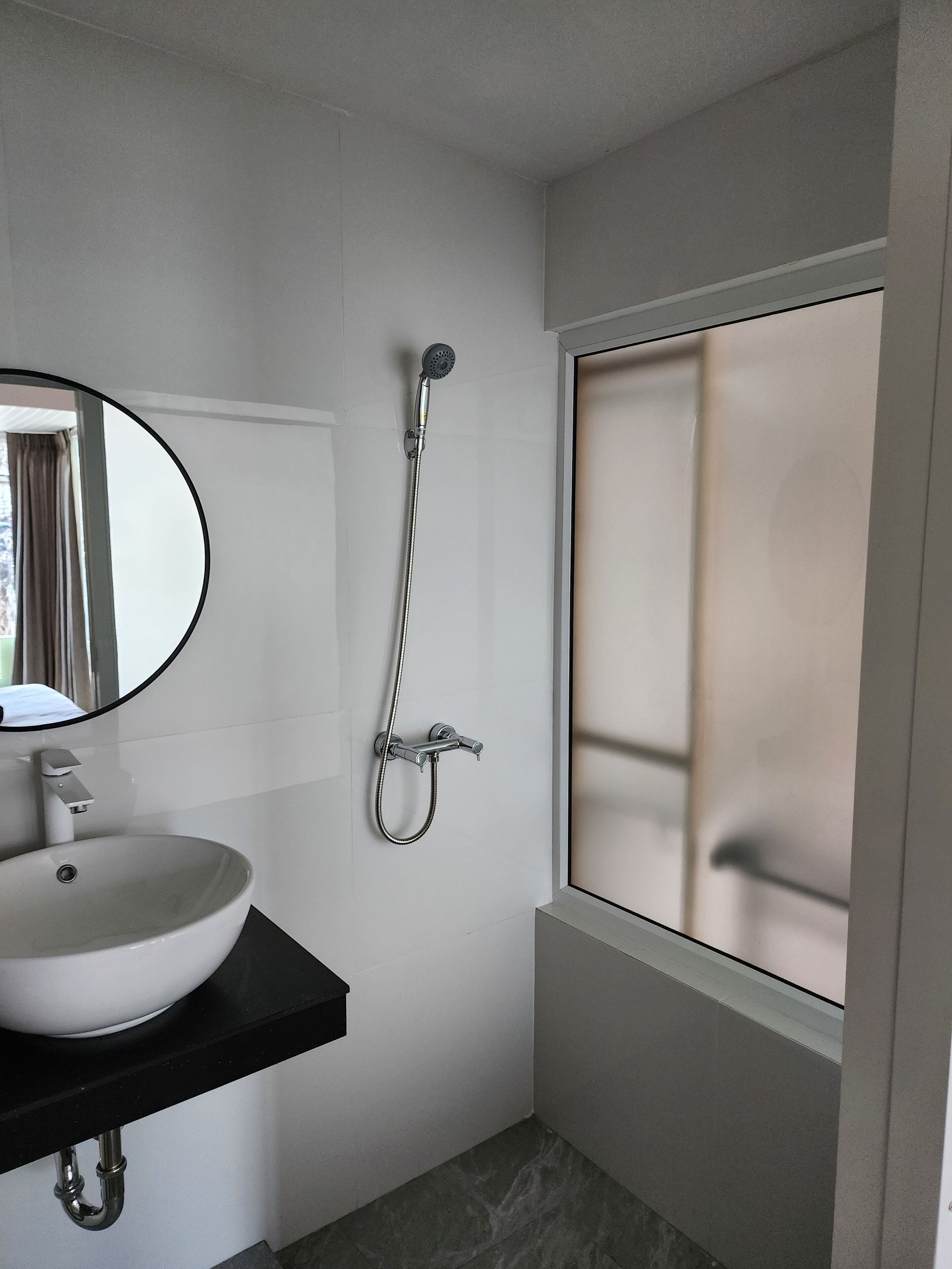 Een badkamer met een wit wastafelmeubel, een spiegel, een douchekop en een raam.