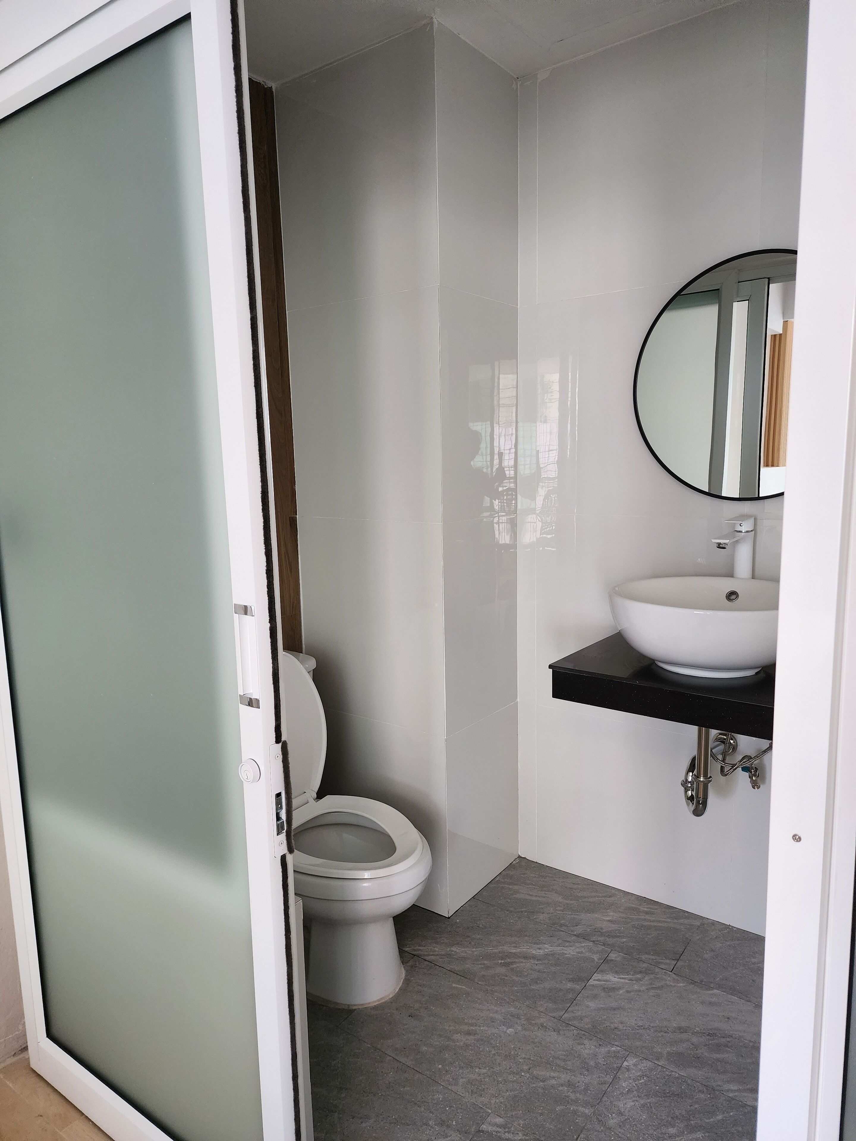 A bathroom with a toilet, a sink with a mirror, and a tiled floor.