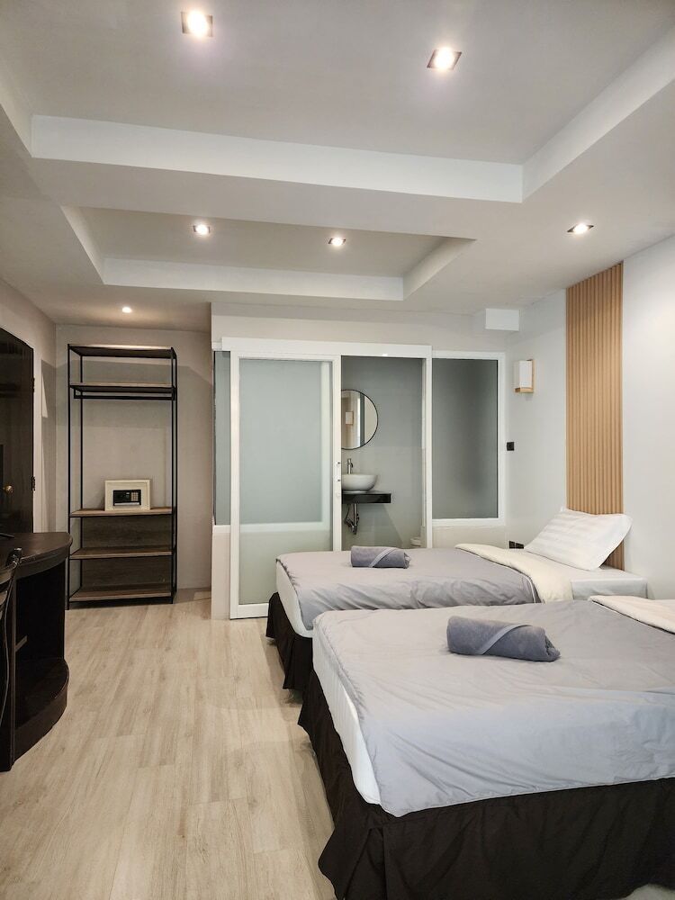 A modern bedroom with two beds, a built-in wardrobe, a mirror, and a small bathroom.