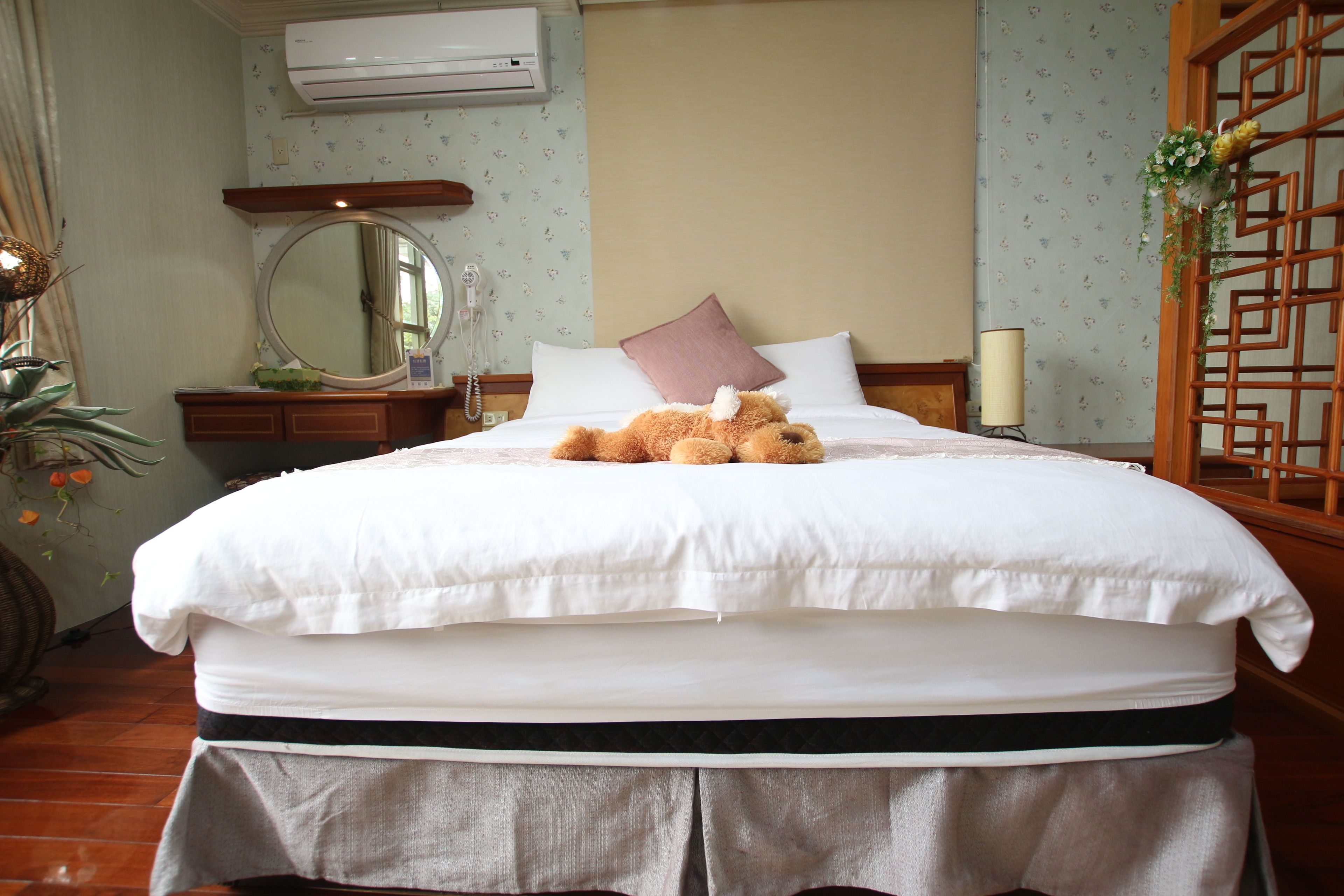 A neatly made bed with a teddy bear, a bedside mirror, and a lamp.