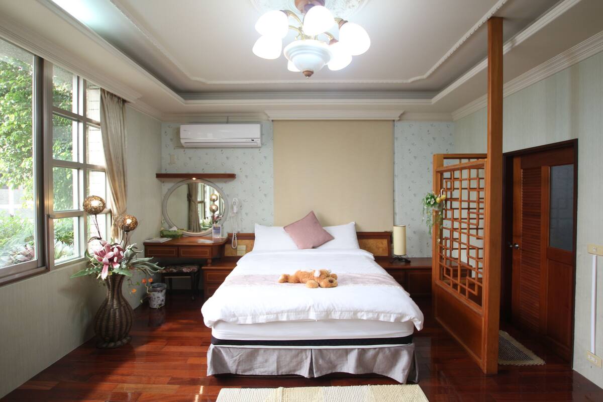 A neatly arranged bedroom with a bed, bedside table, and a large window.