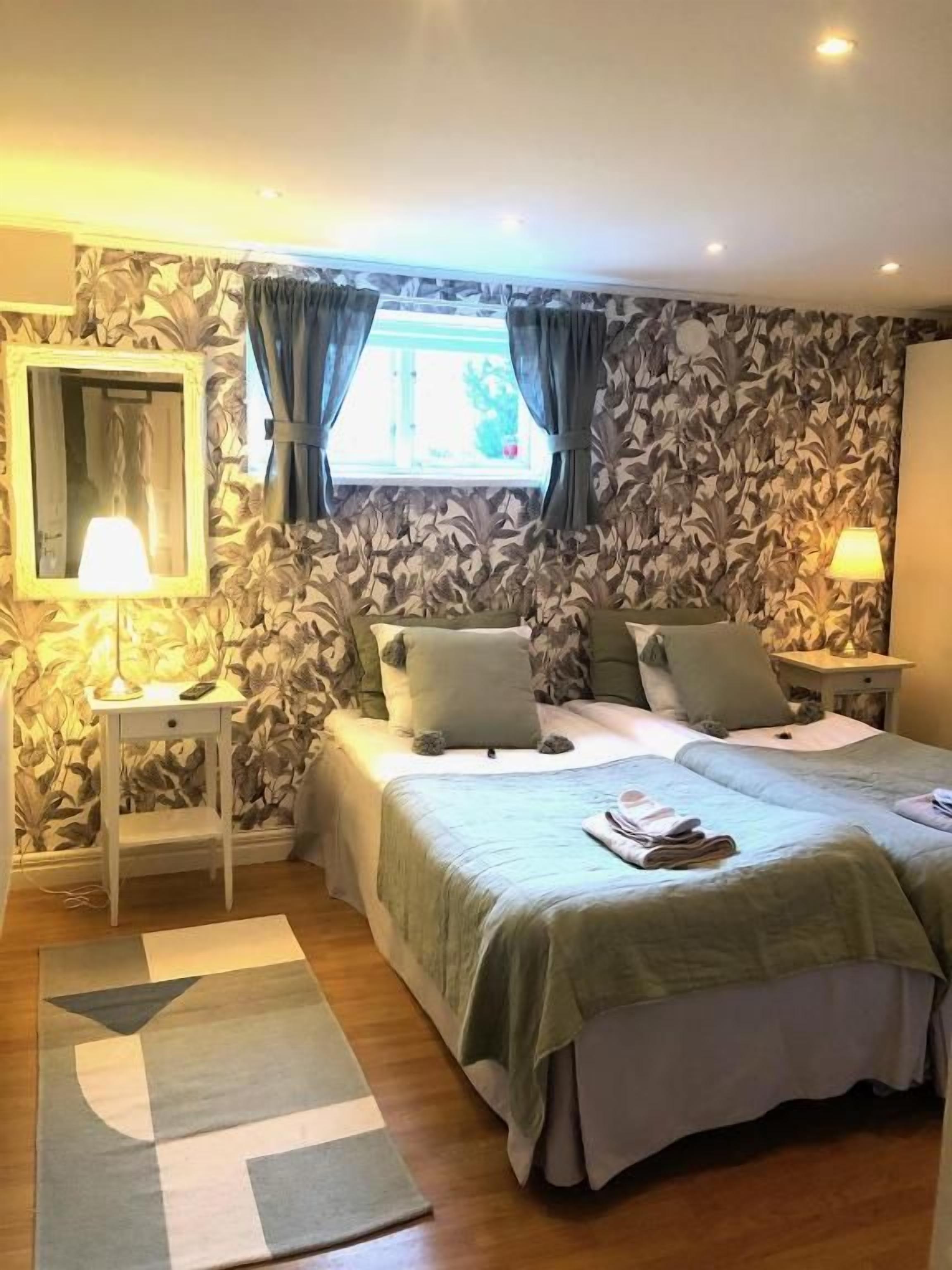 A bedroom with a double bed, a nightstand, a lamp, and a window with curtains.
