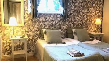 A bedroom with a double bed, a nightstand, a lamp, and a window with curtains.