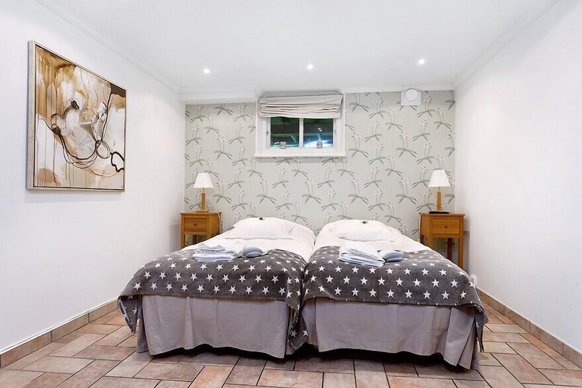 A bedroom with two beds, a window, and a wall-mounted artwork.