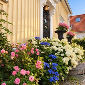 A building with a black door, a light fixture above it, and a potted plant with pink flowers to the right. - 5:ans Bed & Breakfast (Gothenburg)