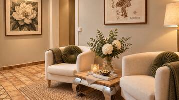 Una habitación con dos sillones, una mesa con un florero y un jarrón, un mapa enmarcado y una lámpara.