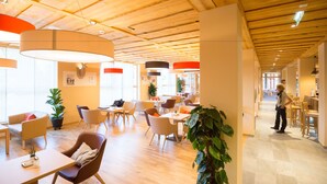 Un espacio interior amplio con suelo de madera, varios arreglos de asientos y grandes ventanales que permiten la entrada de luz natural.