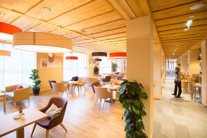 Un espacio interior amplio con suelo de madera, varios arreglos de asientos y grandes ventanales que permiten la entrada de luz natural.