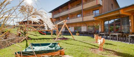 A modern building with a wooden facade, outdoor seating area, and a grassy courtyard.