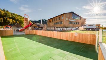 A modern building with a wooden facade, a red slide, and a green artificial turf area.