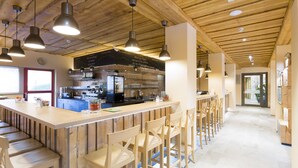 Zona de bar con taburetes de madera, iluminación colgante y una barra con una máquina de café.