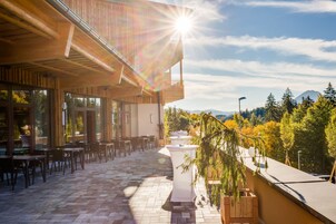 Un patio al aire libre con mesas y sillas, techo de madera y vistas a árboles y montañas al fondo.