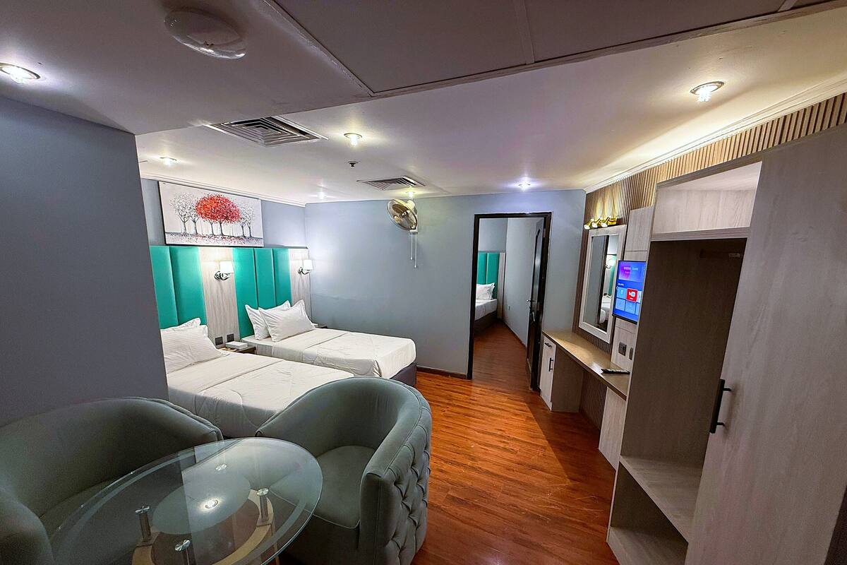 A hotel room with two beds, a glass table, a TV, and a bathroom visible through an open door.