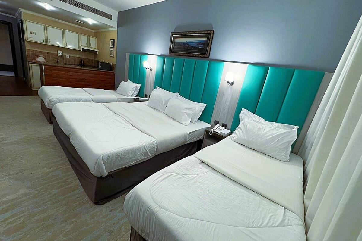 A hotel room with three beds, a kitchenette, and a bathroom.