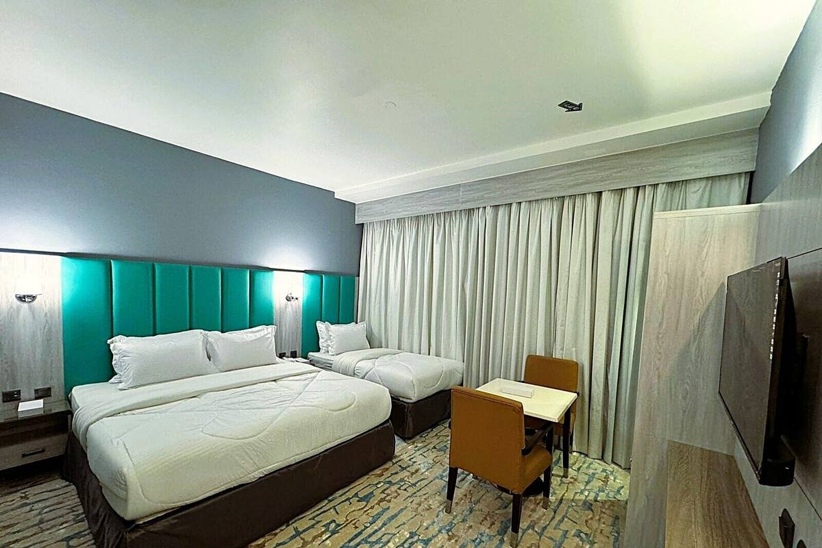 A hotel room with two beds, a desk, a chair, a TV, and a large window with curtains.