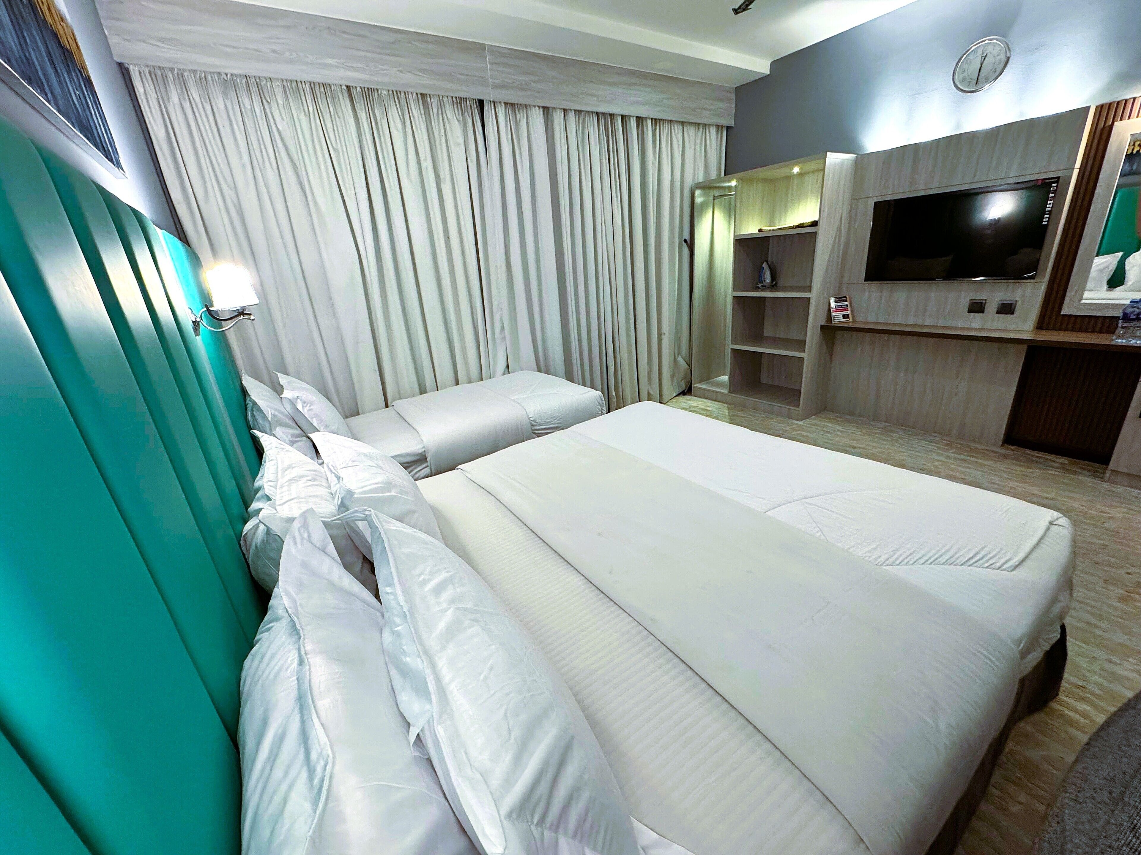 A hotel room with two beds, a TV, a wardrobe, and a curtain.