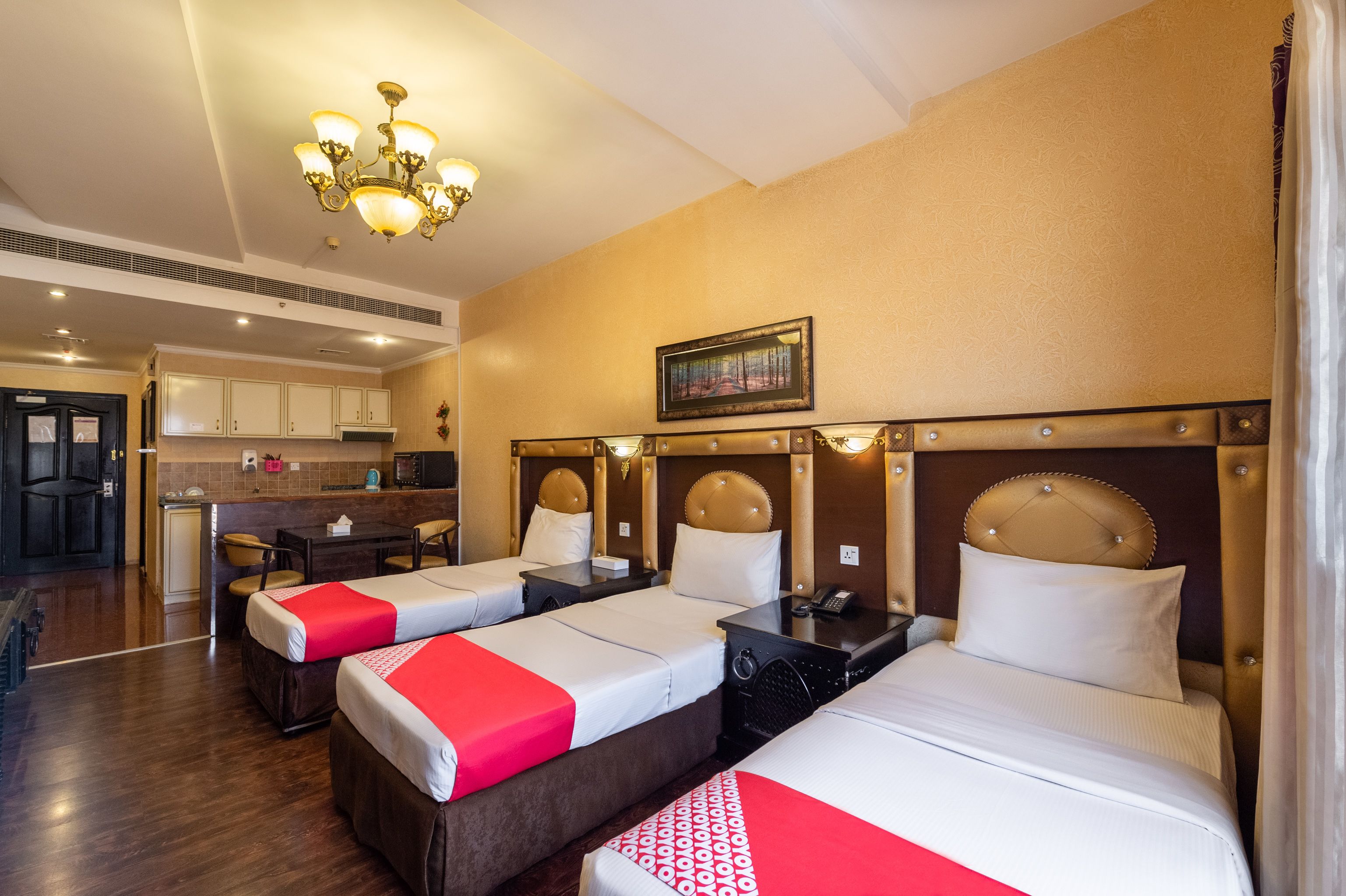 A hotel room with three beds, a dining table, and a kitchen area.