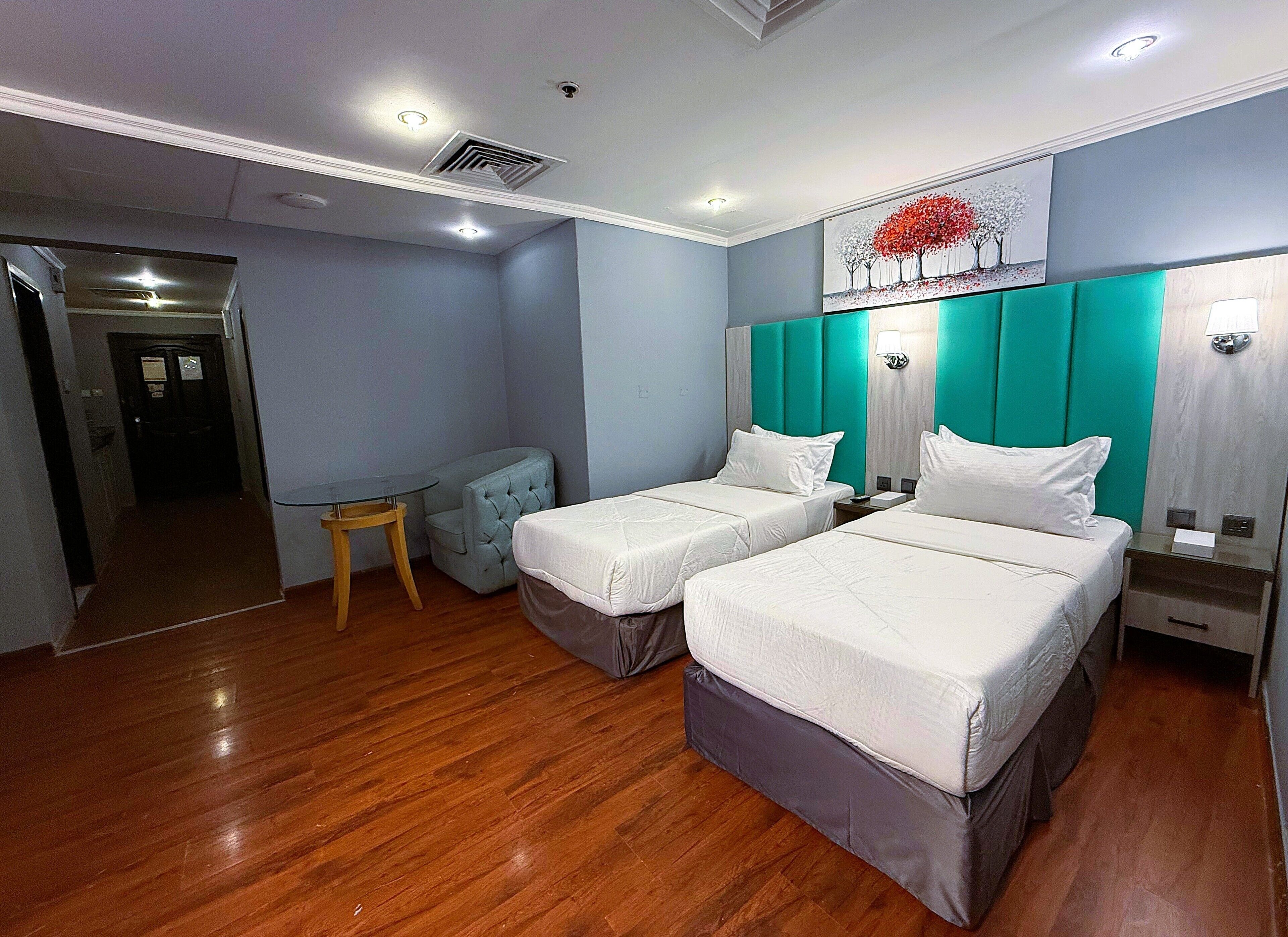 A hotel room with two beds, a small table, a chair, and a painting on the wall.