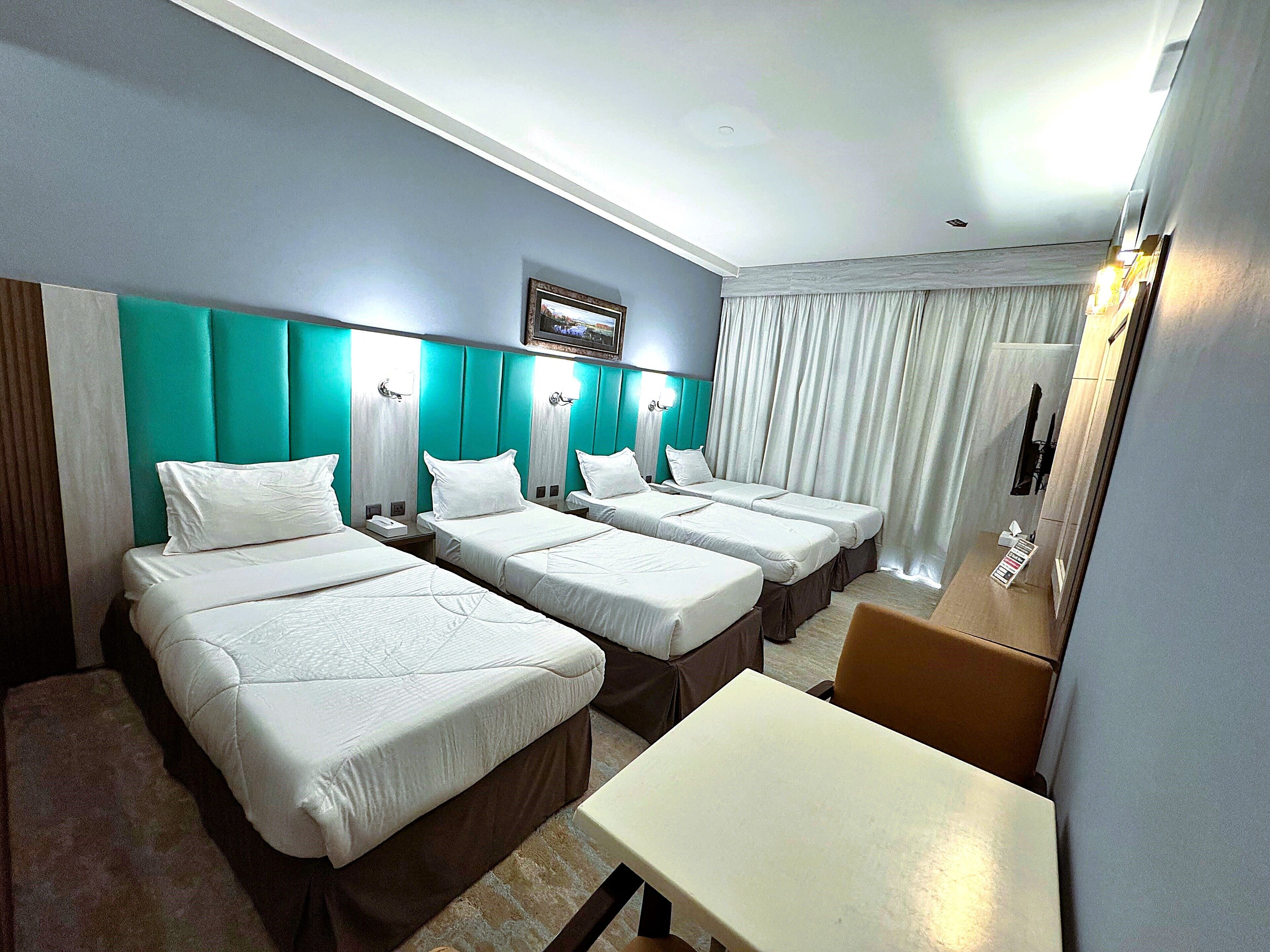 Une chambre d’hôtel avec trois lits, une petite table et un miroir.