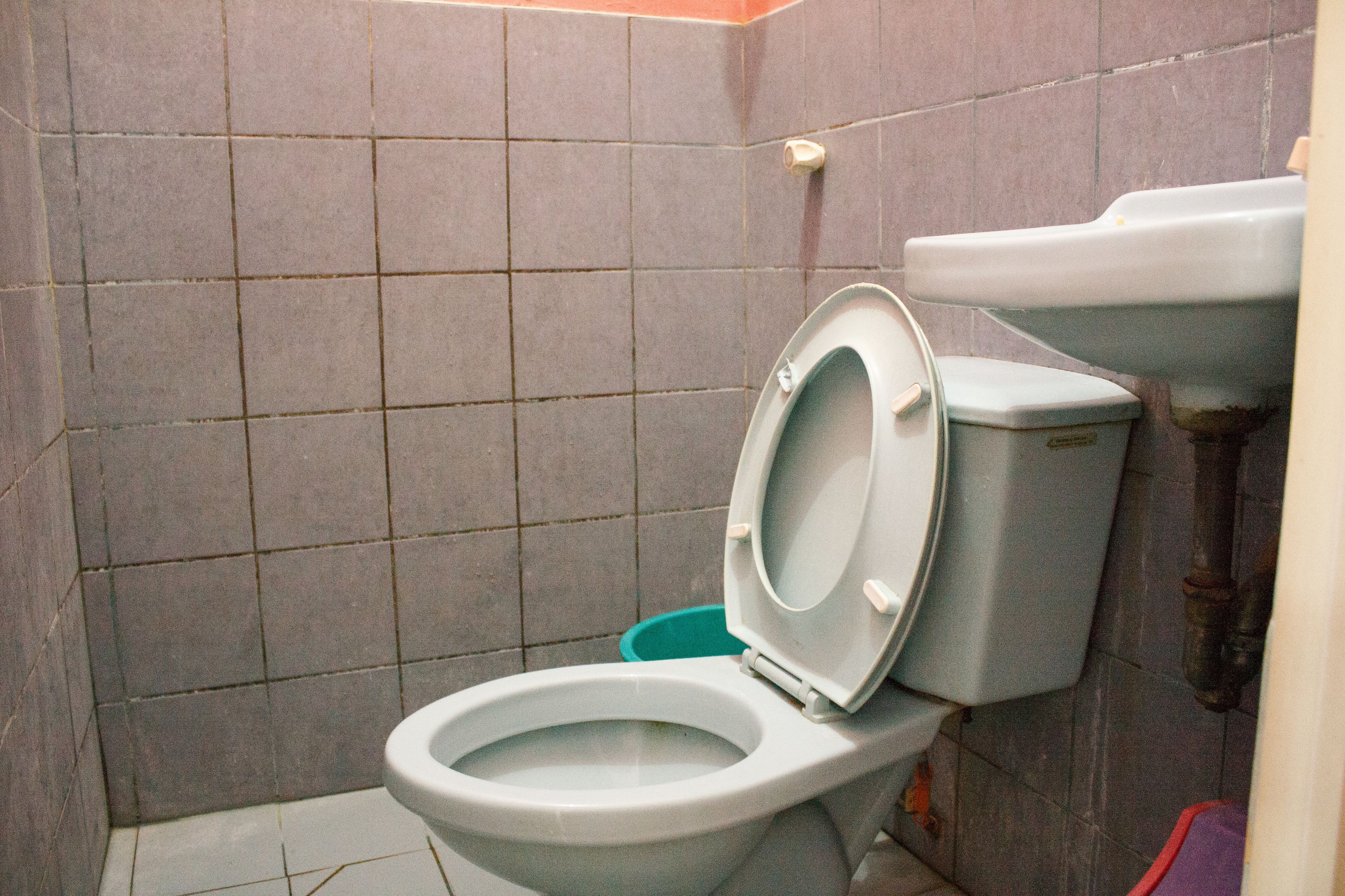 A standard bathroom with a toilet, a green trash bin, and tiled walls.